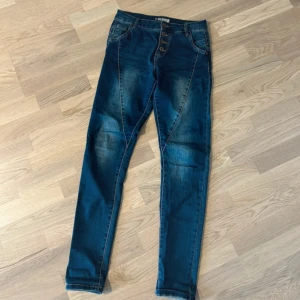 Blå jeansbyxor med knappar - Snygga blå jeansbyxor med en tight passform och dekorativa knappar framtill. Perfekta för en stilren look.
