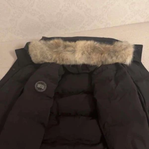 Svart dunjacka med pälsdetalj - Säljer en svart dunjacka från Canada Goose med avtagbar huva och pälsdetalj. Jackan har en klassisk design med dragkedja och knappar framtill. Perfekt för kalla vinterdagar. Äkta såklart kvitto finns, pris kan diskuteras 