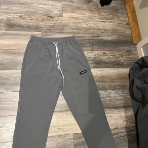 Två byxor för ett pris  - Snygga grå mjukisbyxor med elastisk midja och vit snörning. Perfekta för en avslappnad stil. Byxorna har en rak passform och en diskret logga på sidan.