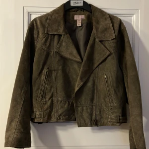 Grön läderjacka från H&M - Säljer en snygg grön läderjacka i bikermodell från H&M. Jackan har en klassisk krage och dragkedjor på fickorna. Perfekt för höst och vår med sin stilrena design. 