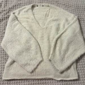 Vit fluffig tröja med v-ringning - Mysig vit tröja med v-ringning och långärmade ärmar. Tröjan har en fluffig textur som ger en extra mjuk känsla. Perfekt för kyligare dagar. Om ni vill se den på, skriv gärna!