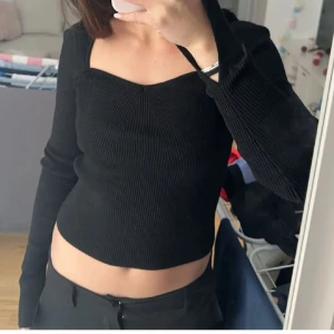 Svart ribbad topp - Snygg svart ribbad topp med långärmad design och en croppad passform. Perfekt för en stilren look. Slitsar i armarna, helt ny!!