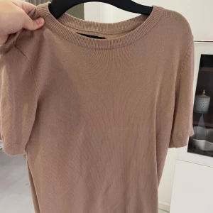 Beige kortärmad tröja - Säljer en stilren beige tröja med korta ärmar. Perfekt för en avslappnad look. Tröjan har en rund halsringning och är tillverkad i ett mjukt material. Köpt i bosnien i en butik 