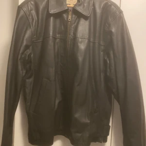 Svart skinnjacka med dragkedja - Snygg svart skinnjacka med dragkedja och klassisk krage. Jackan har långa ärmar och praktiska fickor framtill. Perfekt för en cool och stilren look.