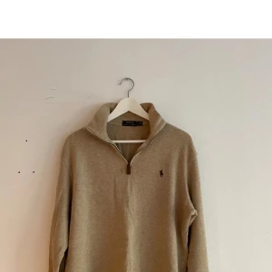 Beige half zip tröja från Polo Ralph Lauren - Säljer en stilren beige half zip tröja från Polo Ralph Lauren med dragkedja och broderad logotyp på bröstet. Perfekt för en avslappnad och snygg look nu under vintern