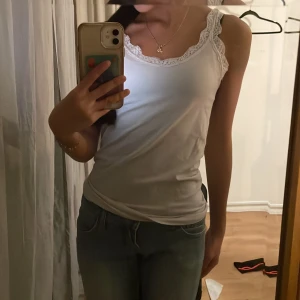 Vit linne med spetsdetaljer - Säljer ett stilrent vitt linne med vackra spetsdetaljer längs axelbanden och halsringningen. Perfekt för en somrig look eller som basplagg i garderoben.