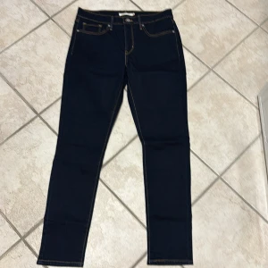 Levi's 311 Shaping Skinny Jeans - Snygga Levi's 311 Shaping Skinny jeans i mörkblå denim. Dessa jeans har en skinny passform och är designade för att forma och framhäva figuren. Perfekta för en stilren look med klassiska femficksdetaljer och guldfärgade sömmar. Midwaist. Helt NYA!