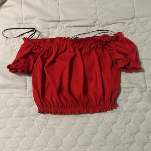 Röd offshoulder topp - Trendig röd offshoulder topp med elastiska kanter och smala axelband. Perfekt för en somrig look.