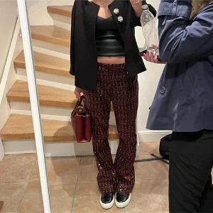 Glittriga byxor i röd och svart - Snygga glittriga byxor i röd och svart med ett rutigt mönster. perfekta för en festlig kväll. De har en bootcut-stil som ger en trendig look.