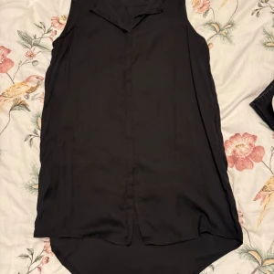 Svart ärmlös blus från mbyM - Snygg svart ärmlös blus från mbyM. Perfekt för en stilren look med en klassisk krage och knäppning framtill. Passar bra till både jeans och kjol.