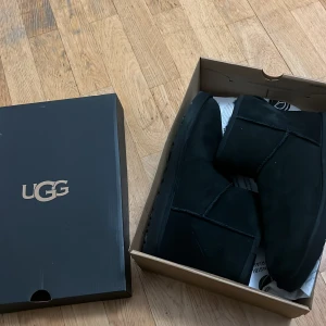 Svarta boots från UGG - Säljer ett par klassiska svarta UGG boots i mjukt material. Perfekta för kyliga dagar med sin varma och bekväma design. Kommer i originalkartong.Storlek 43