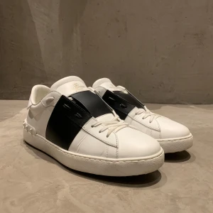 Valentino open - Snygga Valentino Garavani sneakers i vitt med svart detalj. Skorna har en unik design med nitar på hälen och snörning framtill. Perfekta för en stilren look. Skicket väldigt bra då dom knappt är använda! Pris ej hugget i sten vid snabb affär! Storlek 42
