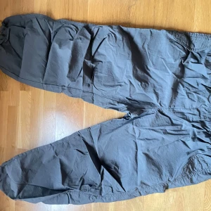 Grå byxor med resår och snörning - Säljer ett par grå byxor med resår i midjan och vid bensluten. Byxorna har en avslappnad passform och är perfekta för en bekväm stil. De är tillverkade i ett lätt material och har praktiska snörningsdetaljer.