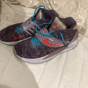 Kd 14  - Snygga Nike sneakers med unikt mönster i grått och brunt. Skorna har en röd Nike-logga och blå snörning. Perfekta för en sportig look.