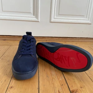 Purplish Blue Christian Louboutin - Snygga blå sneakers från Christian Louboutin med den ikoniska röda sulan. Skorna har snörning och är tillverkade i ett elegant material som ger en lyxig känsla. Perfekta för att ge din outfit en exklusiv touch. Passar folk runt storlek 40-41.5