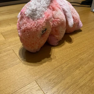 Rosa enhörning från Pillow Pets - Mysig och fluffig rosa enhörning från Pillow Pets. Perfekt som både kudde och gosedjur. Den har en mjuk, lockig man och en söt design med broderade ögon. Enhörningen kan enkelt vikas ut till en kudde för extra komfort.