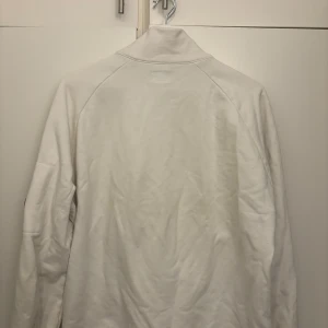 Vit fleecejacka med dragkedja - Säljer en vit fleecejacka med dragkedja och hög krage. Jackan har långa ärmar och praktiska fickor med dragkedjor. Perfekt för kyliga dagar.