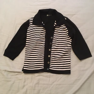 Svart och vit randig kofta - Snygg svart och vit randig kofta med trekvartsärmar och knappar framtill. Perfekt för en stilren look.