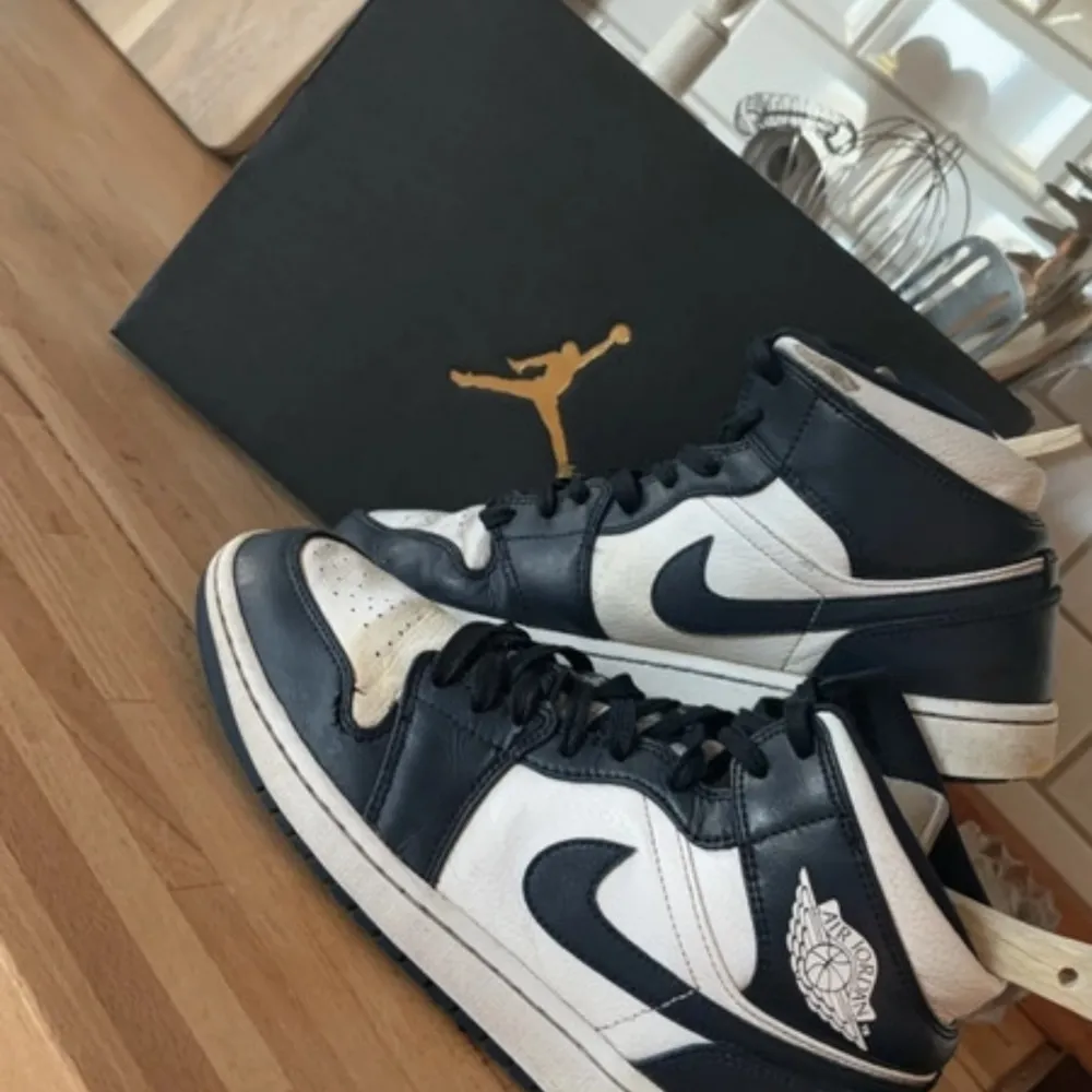 Säljer ett par Nike Air Jordan 1 Mid i mörkblå och vit. Skorna är i nyskick och kommer med originalkartong. De har en klassisk design med snörning och är perfekta för både vardag och fest. Storlek herr 42,5 (EUR).. Skor.