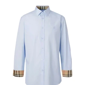 Ljusblå skjorta med rutiga detaljer - Säljer en stilren ljusblå skjorta från Burberry. Den har långa ärmar och klassiska knappar framtill. Detaljerna vid ärmsluten är i det ikoniska Burberry-rutiga mönstret. Perfekt för både vardag och fest! Orginl pris 5000kr