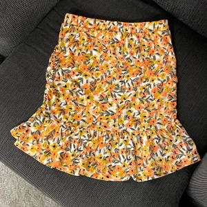 Blommig kjol från Vila - Säljer en färgglad blommig kjol från Vila i storlek XS. Kjolen har ett vackert mönster i orange, gul och svart med volangdetaljer vid fållen. Den är använd 2 eller 3 gånger ser ut som ny. Kontakta mig för frågor 😍😍🦋✨