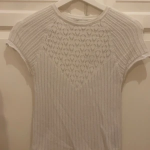 Vit ribbad topp från Zara - Säljer en vit ribbad topp med korta ärmar och ett snyggt mönster framtill. Toppen är croppad och har en tight passform