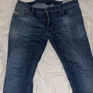 Blå jeansbyxor från Diesel - Snygga blå jeansbyxor från Diesel med knappgylf och klassisk femficksdesign. Perfekta för en avslappnad stil med en touch av edge.
