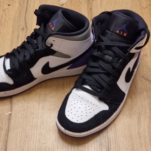 Nike Air Jordans i svart, vitt och lila - Snygga Nike Air Jordans med en klassisk design i svart, vitt och lila. Skorna har snörning och en hög siluett med en kombination av skinn och mocka. Perfekta för dig som vill ha en stilren och sportig look.