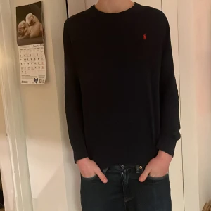 Svart tröja från Polo Ralph Lauren - Säljer en stilren svart tröja från Polo Ralph Lauren med det klassiska röda logotypen på bröstet. Tröjan är långärmad och tillverkad i mjuk bomull, ett litet hål i vönster armhåla bara skriv om bilder. En xl i barnstorlek så S i herrstorlek