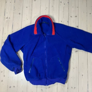 80-90 tal Columbia två jackor i ett - Skidjacka! - Unik vintage Columbia skidjacka från 80–90-talet! En tidlös röd vind- och regntålig mjuk skaljacka i kombination med en avtagbar blå fleece innerjacka. Den här mångsidiga jackan är både funktionell och stilsäker – bär jackorna tillsammans för maximal värme och skydd, eller använd dem separat beroende på väder och behov.  Med långa ärmar, praktiska fickor med dragkedjor och den klassiska kvaliteten som Columbia är känt för, är detta det perfekta valet för både vardag och friluftsliv.