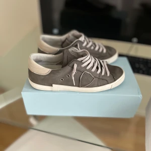 Grå sneakers från Philippe Model - Snygga grå sneakers från Philippe Model med vita detaljer och snörning. Skorna har en stilren design med en kontrasterande vit sula och en diskret logotyp på sidan. Storlek 40 men passar 41/42