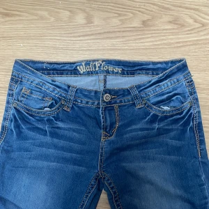 Bootcut Lowwaist jeans från Wallflower - Snygga blå bootcut jeans från Wallflower med klassisk femficksdesign och dekorativa sömmar på bakfickorna. Tillverkade i en bekväm blandning av bomull, polyester och spandex för extra stretch. Perfekta för en avslappnad stil. Knappt använda.