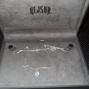 Smyckeset från Kejsar - Elegant smyckeset från Kejsar med ett halsband och ett armband. Halsbandet har en glittrig kedja med en droppformad hängande sten. Armbandet är en klassisk tennisarmband-design med gnistrande stenar. Perfekt för att lägga till lite glamour till din look. 700kr/st