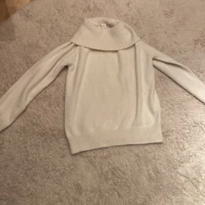 Beige/vit stickad polotröja från Lindex - Mysig beige/vit stickad polotröja från Lindex Kids. Perfekt för kyliga dagar med sin höga krage och långa ärmar. Tröjan har ribbade detaljer vid krage, ärmslut och nederkant.