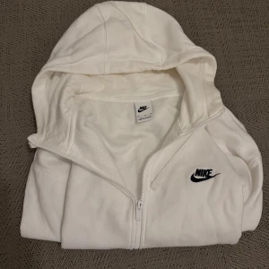 Vit hoodie från Nike - Säljer en stilren vit hoodie från Nike med dragkedja och huva. Perfekt för en avslappnad look. Den har en klassisk Nike-logga på bröstet🙌 Inte använd ofta alls, med snabb affär kan priset ändras😆