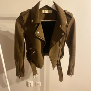 Brun mockajacka från Zara - Snygg brun mockajacka från Zara med dragkedja och bälte. Jackan har en klassisk bikerstil med långa ärmar och axelklaffar. Perfekt för en cool och stilren look.
