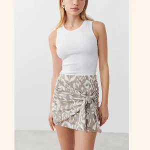 Beige omlottkjol med mönster - Trendig beige omlottkjol med ett subtilt mönster och knytning framtill. Perfekt för varma dagar och ger en chic touch till din outfit. aldrig använd 