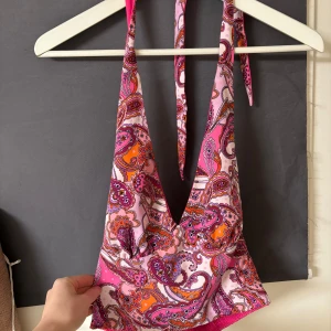 Färgglad paisleymönstrad halterneck topp - Säljer en snygg halterneck topp med paisleymönster i rosa, orange och vitt. Toppen har en djup v-ringning och knytband i nacken. Perfekt för sommarens alla tillfällen!