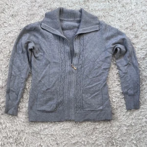 Stickad Cardigan  - Mysig grå kofta med dragkedja och ribbad krage. Den har två praktiska fickor framtill och ett diskret mönster längs dragkedjan. Perfekt för kyliga dagar. Skriv vid minsta fundering, vid snabb och smidig kan pris diskuteras!!! Mvh Edde 