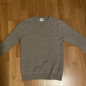 Beige kashmirtröja från John Henric - Säljer en stilren grå kashmirtröja från John Henric. Tröjan har en klassisk rund hals och långa ärmar, perfekt för kyligare dagar. Den mjuka kashmiren ger en lyxig känsla och passar perfekt både till vardags och speciella tillfällen. Den köptes för 2200kr och har knappt använt den pågrund av att jag växte ur den snabbt. Tröjan har storlek XS men passar även S