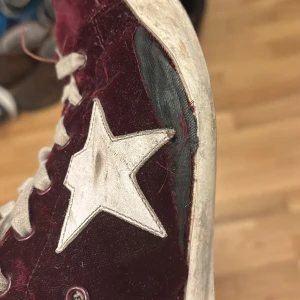 Vinröda sneakers från Golden Goose - Säljer ett par vinröda sneakers från Golden Goose med en vit stjärndetalj på sidan. Skorna är i riktigt dåligt skick och behövs tas till en skomakare eller repareraras. Dustbag och låda med kommer vid köp av skorna. Skriv innan ni köper skorna/ skriv vid minsta fundering.