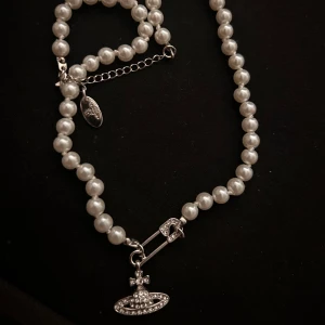 Pärlhalsband  Vivienne Westwood - Elegant pärlhalsband från Vivienne Westwood med ikonisk orb. Äldre modell från 2020. Halsbandet har en säkerhetsnål som detalj och justerbar kedja för perfekt passform. Perfekt för att ge som julklapp eller liknande.   Pris går att diskutera