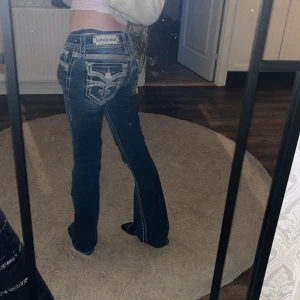 Mörkblå jeans från Rock Revival - Obs-söker byten i storlek W24/25, XS.           Snygga mörkblå jeans från Rock Revival med unika broderade detaljer och nitar på bakfickorna. Jeansen har en bootcut passform och är lågmidjade.