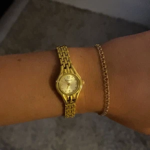 Guldfärgad klocka med länkarmband - Elegant guldfärgad klocka med ett detaljerat länkarmband. Klockan har en rund urtavla med tydliga siffror och en klassisk design. Perfekt för att ge en lyxig touch till din stil.