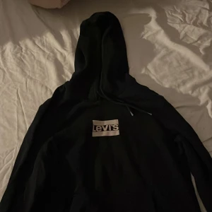 Svart hoodie från Levi's - Säljer en svart hoodie från Levi's med klassisk logga på bröstet. Perfekt för en avslappnad stil med sin bekväma passform och huva. Ett måste i garderoben för alla som älskar streetwear.