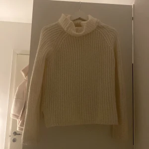 Vit stickad polotröja - Mysig vit stickad polotröja med ribbad design och långa ärmar. Perfekt för kyliga dagar med sin höga krage som håller dig varm. En klassisk och stilren tröja som passar till många olika outfits.