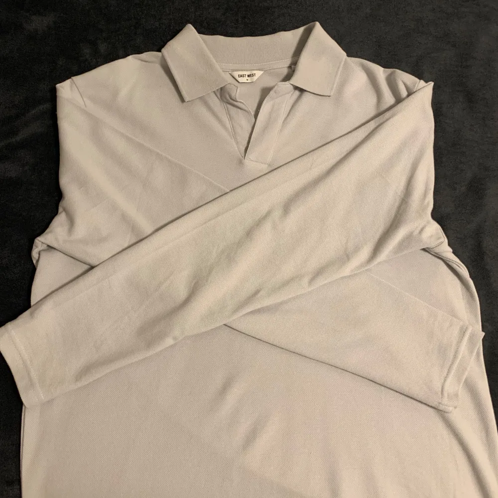 Säljer en stilren ljusgrå pikétröja från Uniqlo. Tröjan har långa ärmar och en klassisk krage. Perfekt för en avslappnad men ändå snygg look.. Neuletakit & Villapaidat.