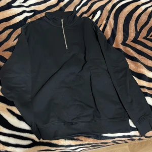 Svart tröja med dragkedja - Säljer en stilren svart tröja med dragkedja i halsen. Perfekt för en avslappnad look. Tröjan har långa ärmar och en hög krage. Storlek M men kan passa L 