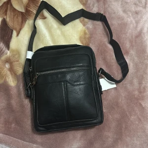 Svart axelväska från Jingpin - Snygg svart axelväska i syntetmaterial från Jingpin. Väskan har flera praktiska fack med dragkedja och en justerbar axelrem för bekväm användning. Perfekt för att hålla dina saker organiserade och lättillgängliga.