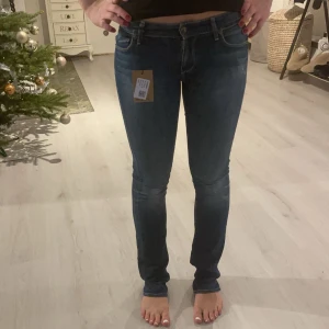 Lågmidjade blå jeans  - Snygga blå jeansbyxor med en tight passform. De har en klassisk femficksdesign och är perfekta för en avslappnad stil. Byxorna har en knapp och dragkedja framtill.